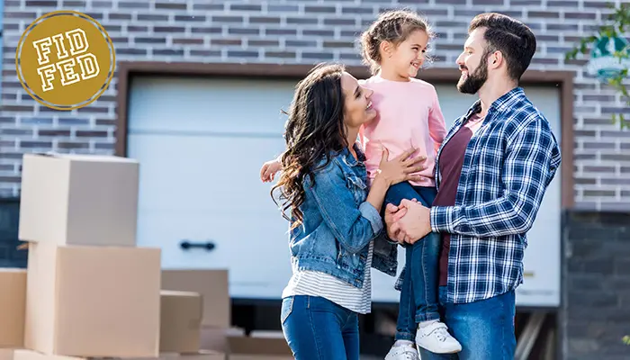 Young couple and daughter in front of their new home with moving boxes by the garage